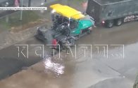 Стоя по колено в воде дорожные рабочие кладут асфальт на дорогу